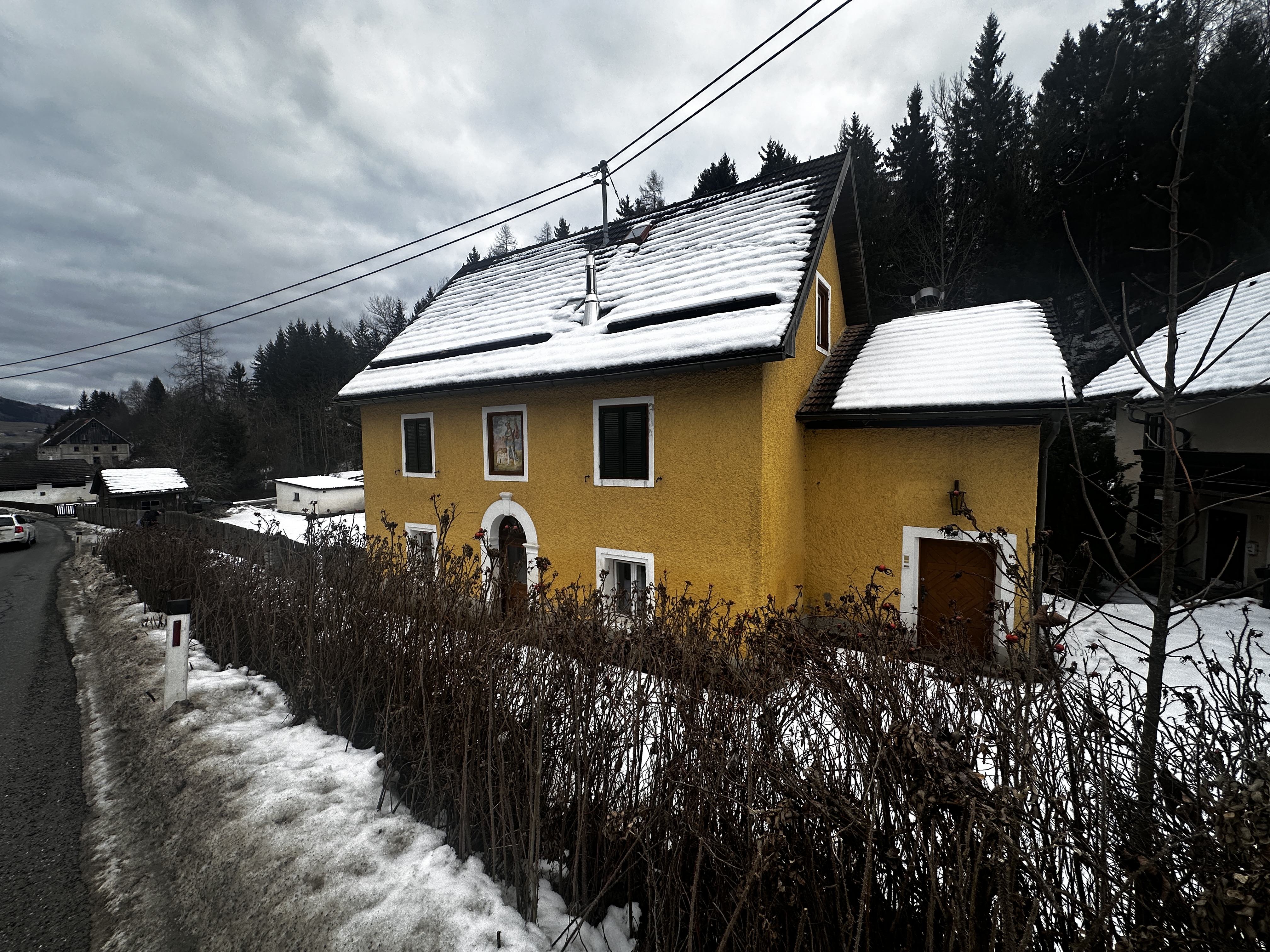 Straßenseitige Fassade mit verschneitem Dach und sichtbaren Freileitungen.