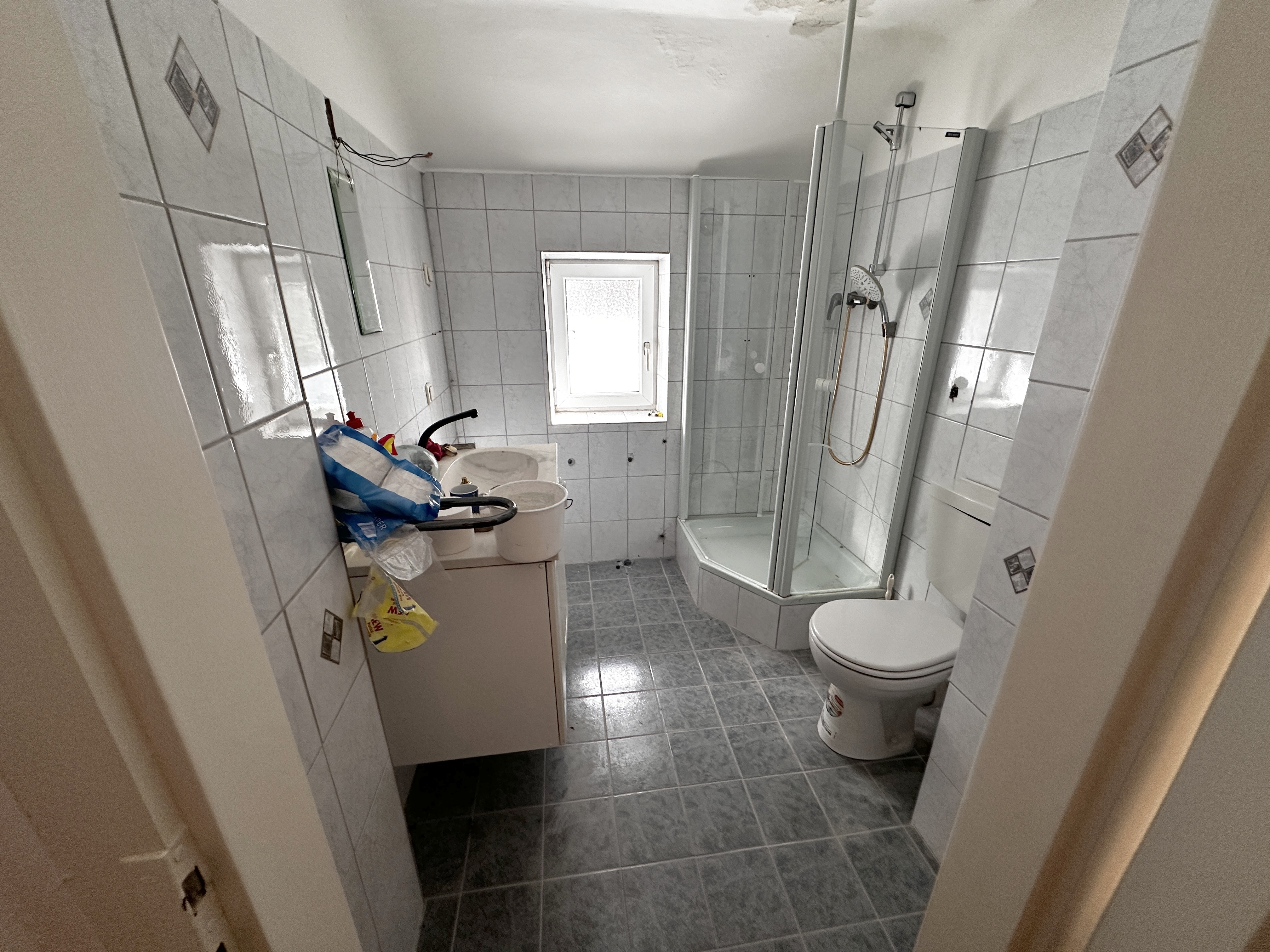 Aufgehellter gefliester Sanitärraum mit Dusche, WC und Waschplatz.