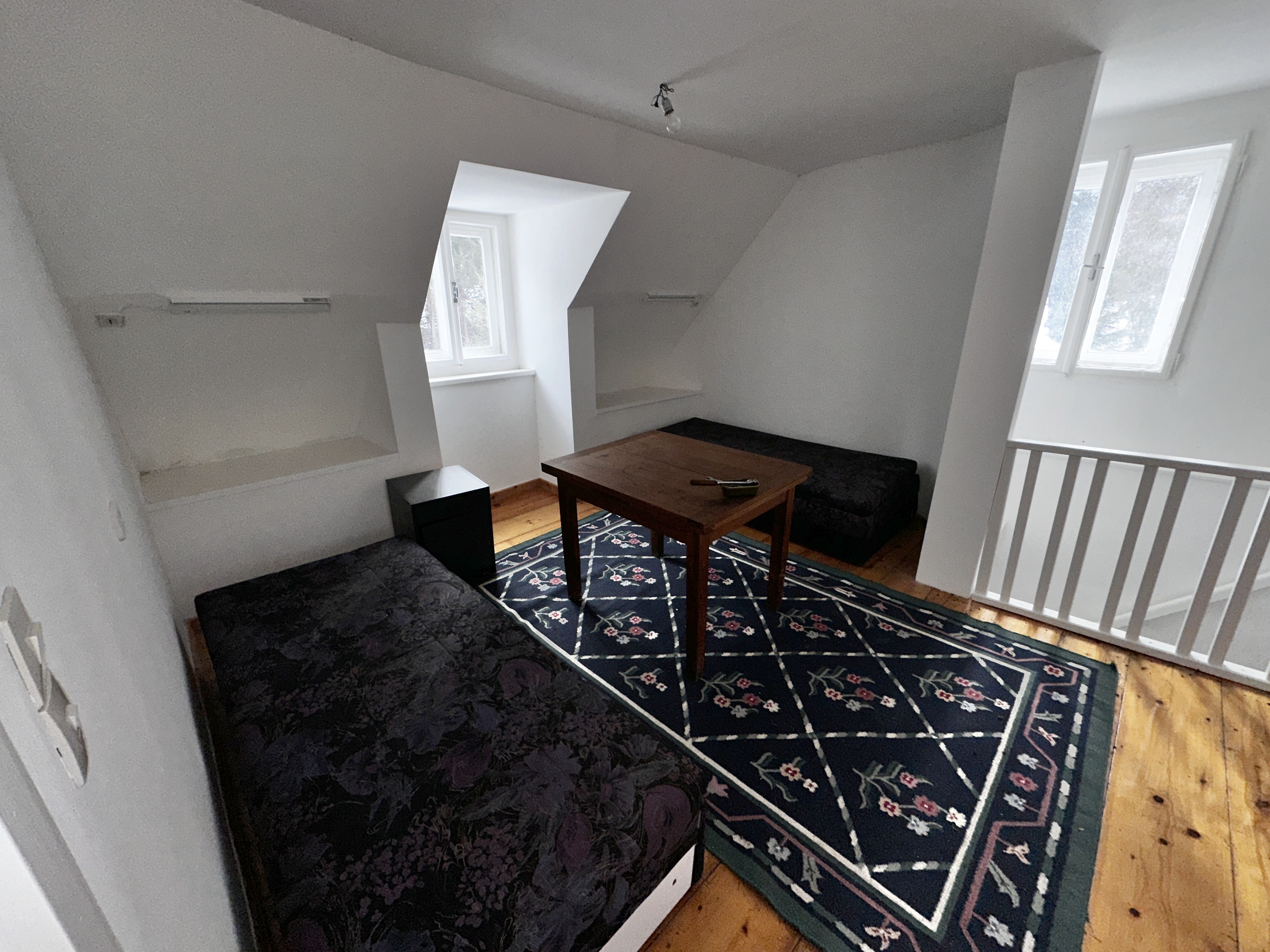 Aufgehellter Dachgeschossbereich mit Sitzmöbeln, Teppich, Tisch und Geländer.
